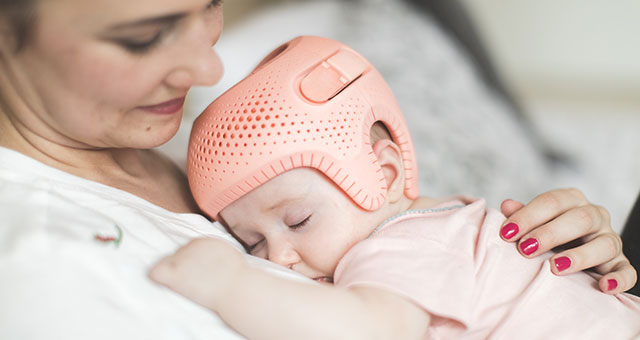 Baby trägt Talee-Helm und schläft auf dem Bauch der Mutter